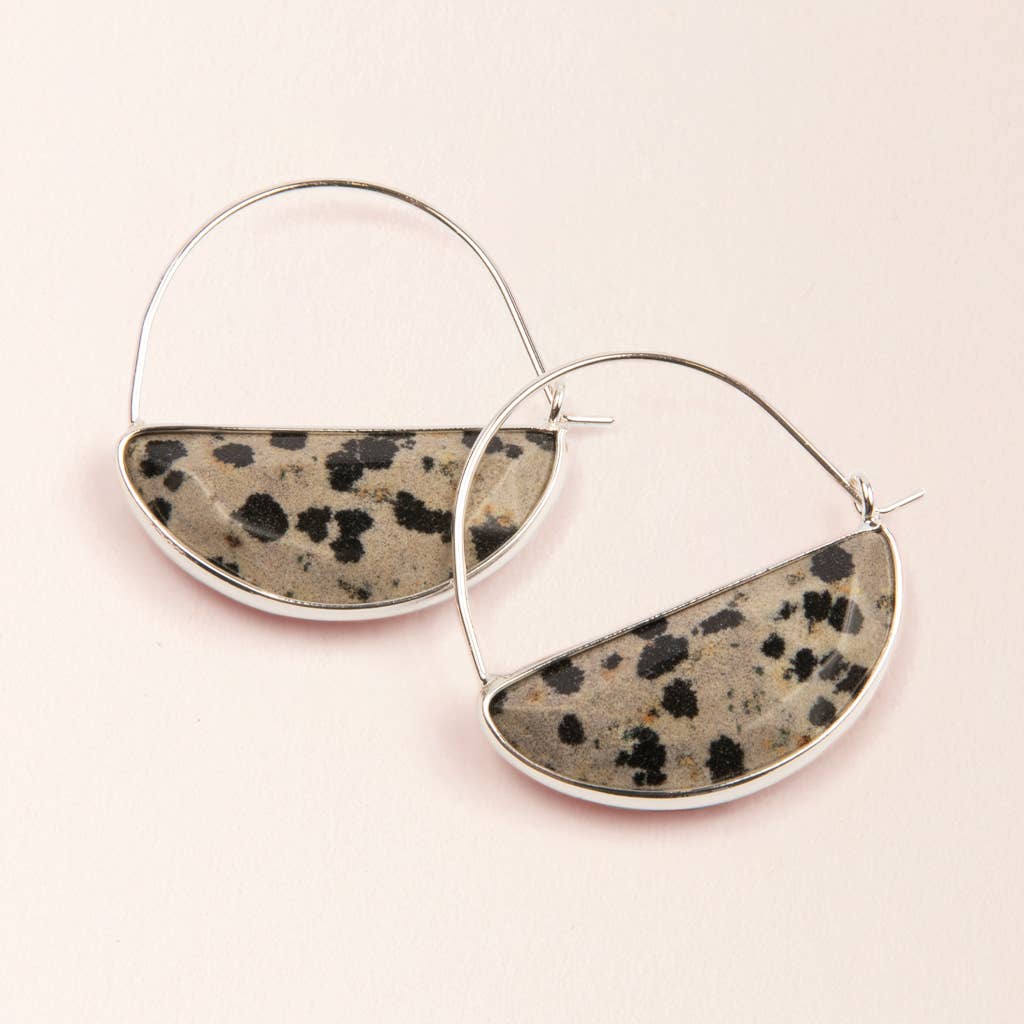 A pair of hoop earrings with a semi-circular dalmatian jasper stone set in a silver-colored frame, displayed against a pink background.