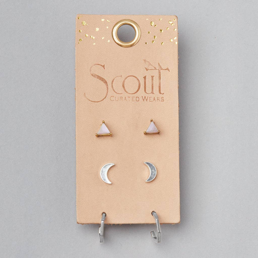 A card with three stud earrings, two with silver finish and one with a rose quartz stone, presented on a leather surface with gold foil accents.