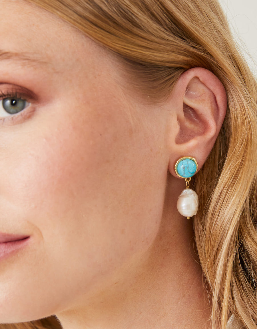 Close-up of a woman wearing an earring with a turquoise stone and pearl.