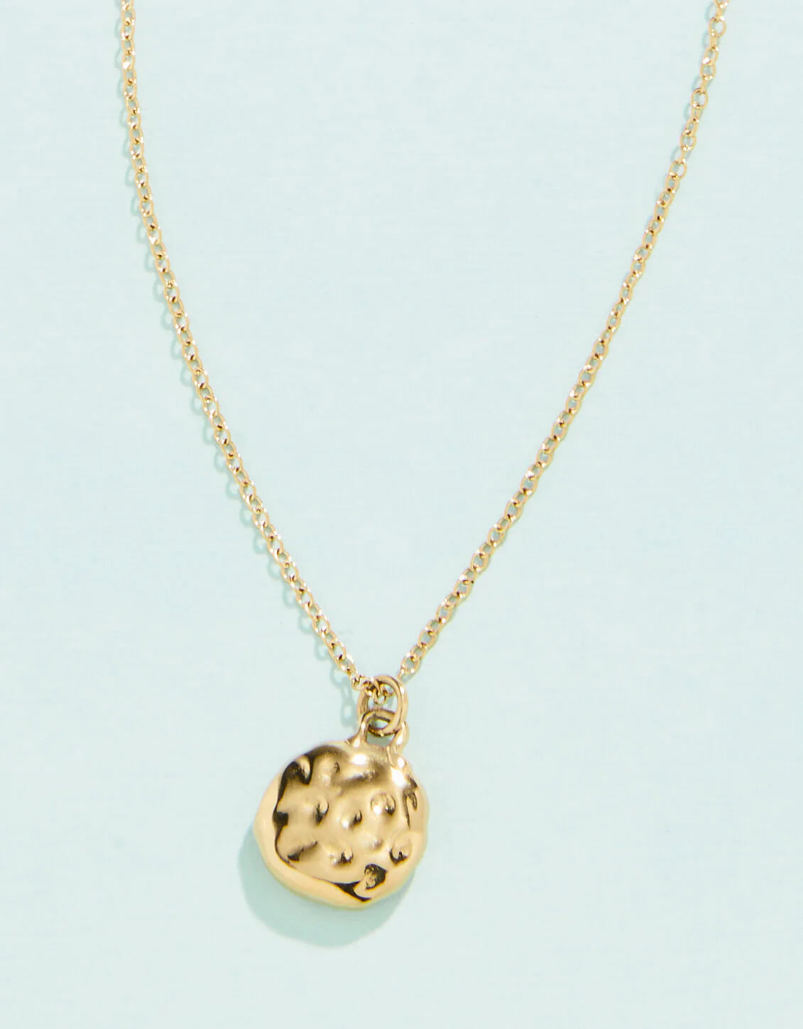 A gold-colored necklace with a textured pendant on a chain, displayed against a white background.