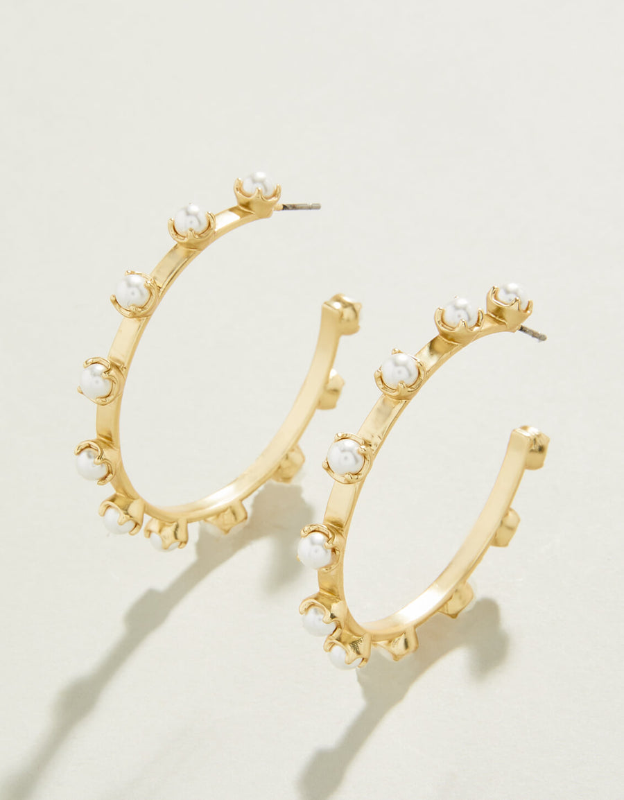 A pair of gold-colored hoop earrings with faux pearl embellishments on a white background.
