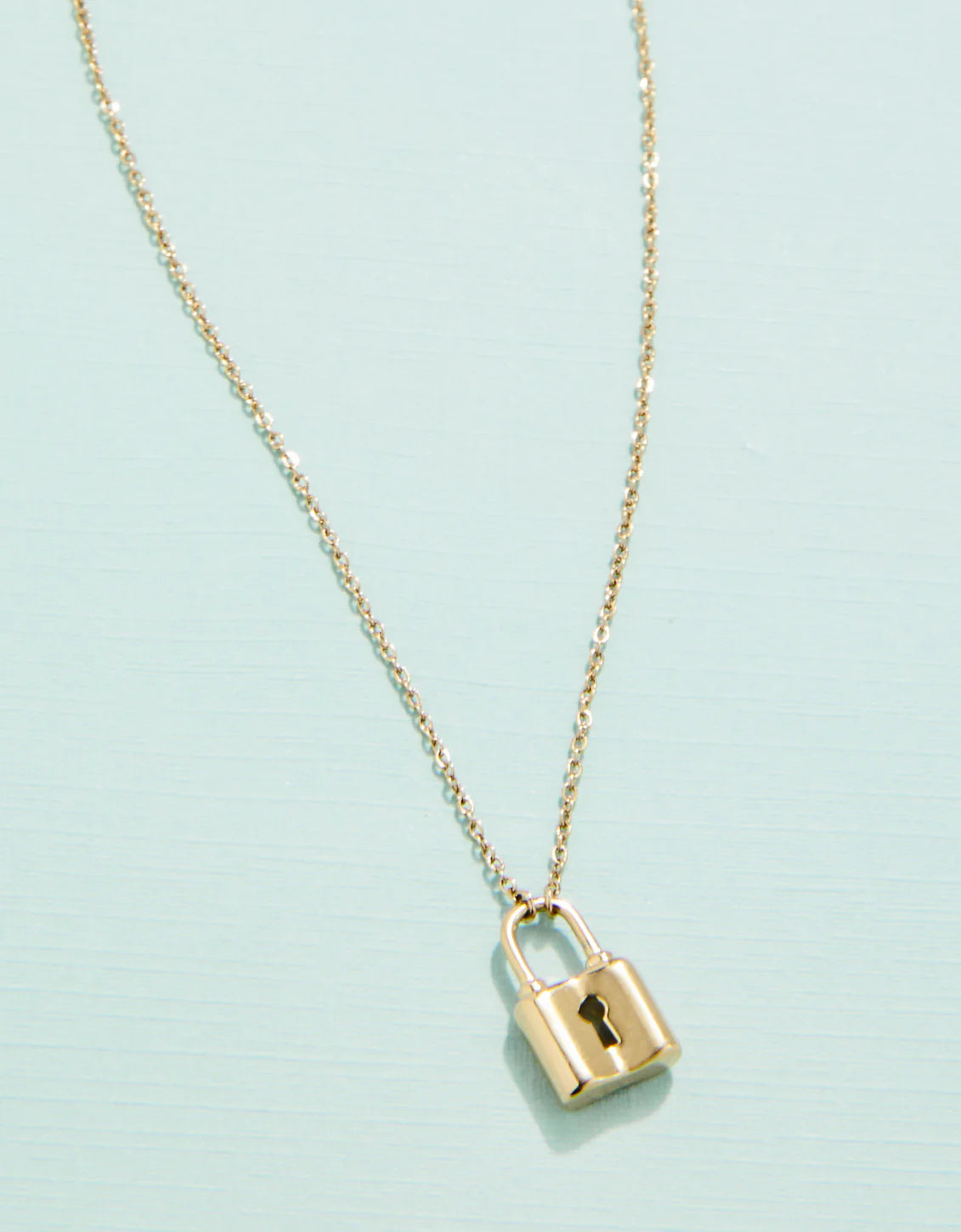 A gold padlock-shaped necklace pendant attached to a delicate chain, set against a light blue background.