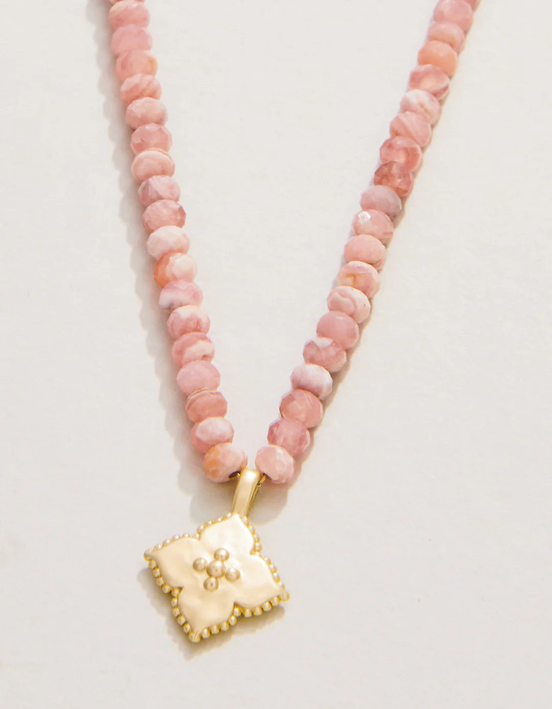 Necklace with pink beads and a gold pendant on a light gray background