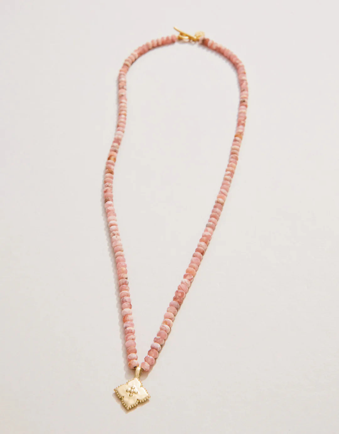 Necklace with pink beads and gold clasp on a light gray background
