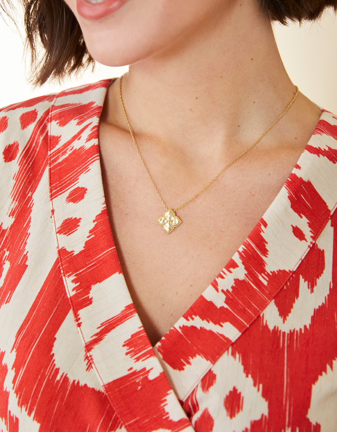 Close-up of a person wearing a gold necklace with a heart pendant, dressed in a red and white patterned garment.