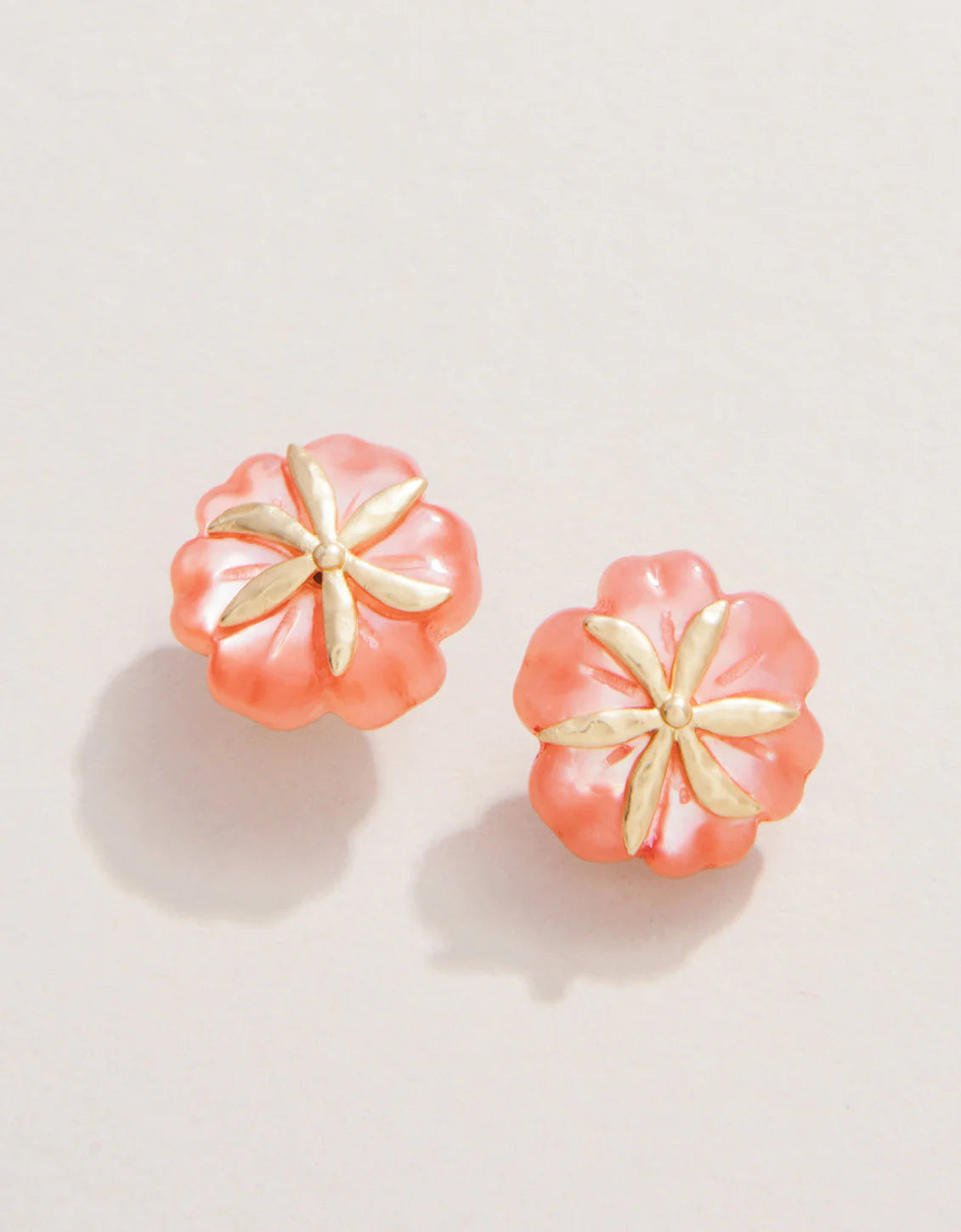 A pair of pink mother-of-pearl flower stud earrings with 18kt matte gold plating on a white background.