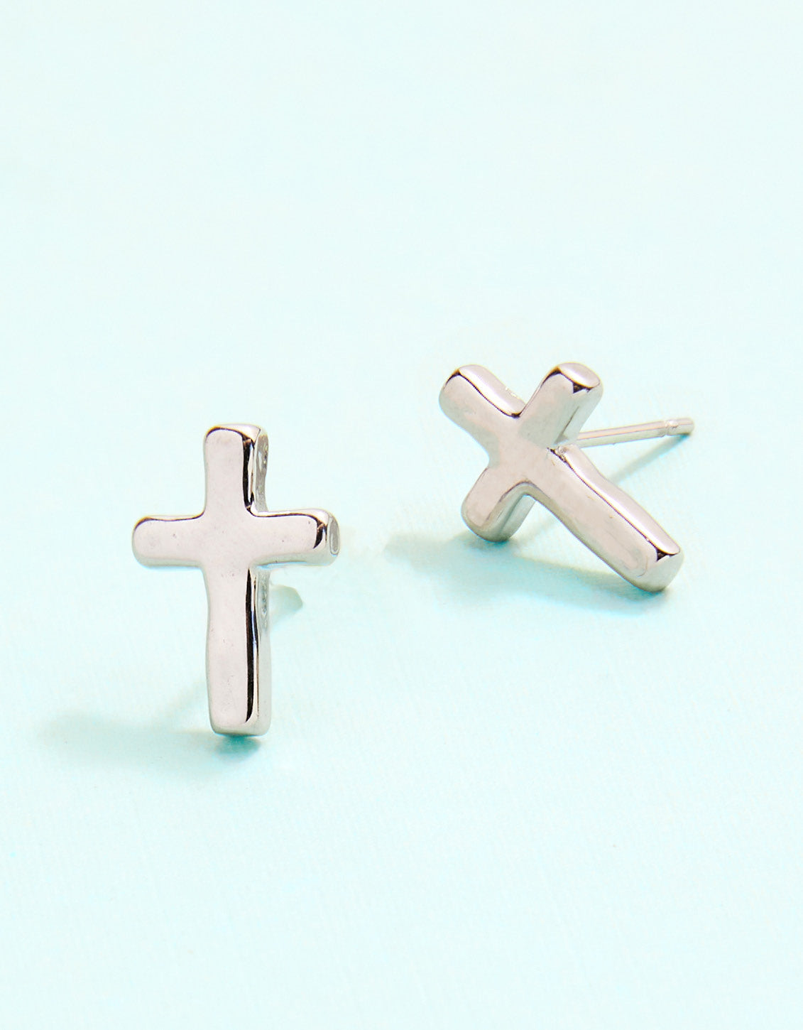 Rose gold cross-shaped earrings on a light blue background