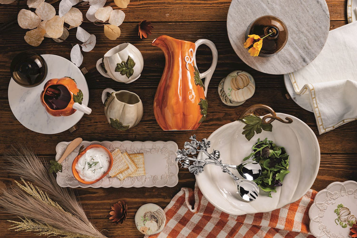 Dining table setting with ceramic pitcher, plates, and cutlery on a wooden surface.