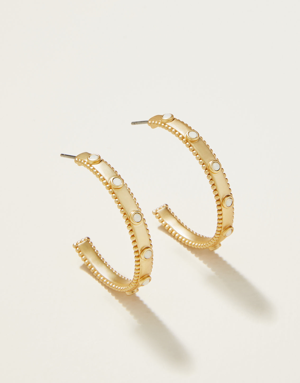 A pair of gold-colored hoop earrings with white opal crystals attached to them, displayed against a white background.