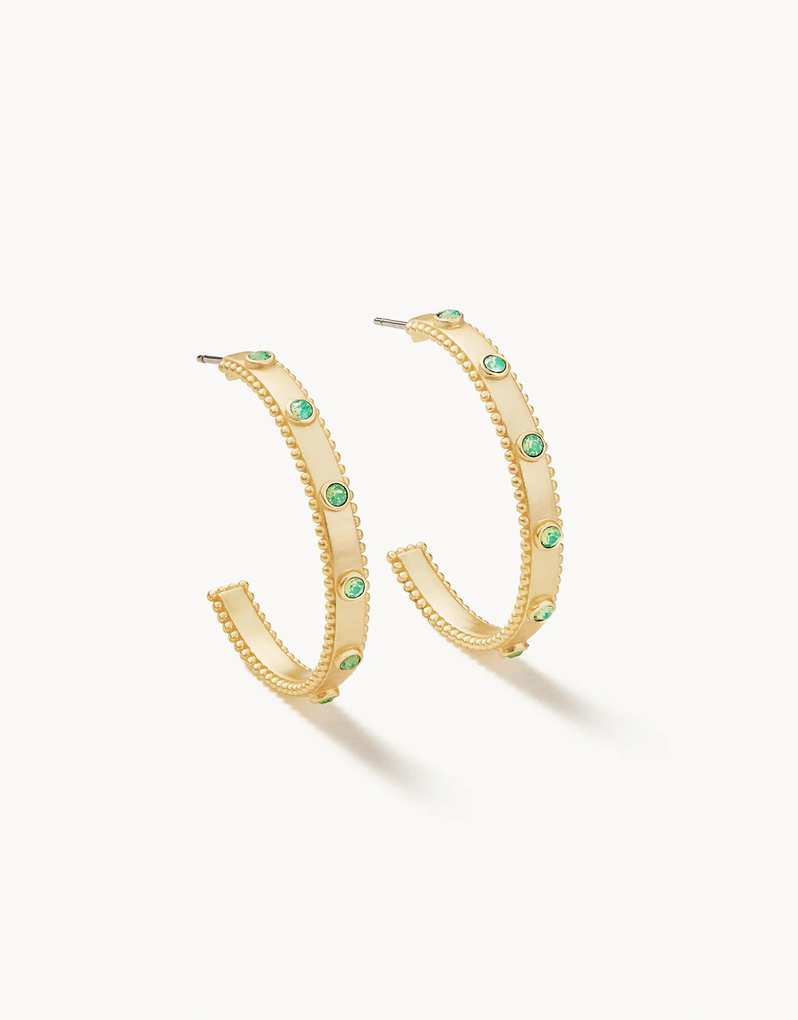 A pair of gold-colored hoop earrings with green Swarovski crystals embedded on the hoop.