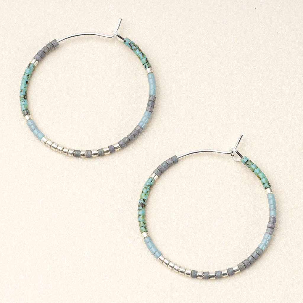 A pair of round hoop earrings with turquoise and silver colors on a white background, made with metallic beads and silver wire.