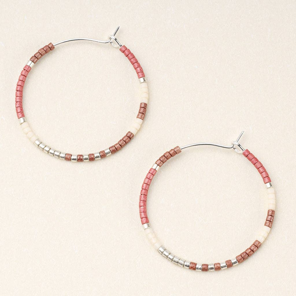 A pair of round hoop earrings with blush multi-colored beads and silver accents, displayed against a beige background.