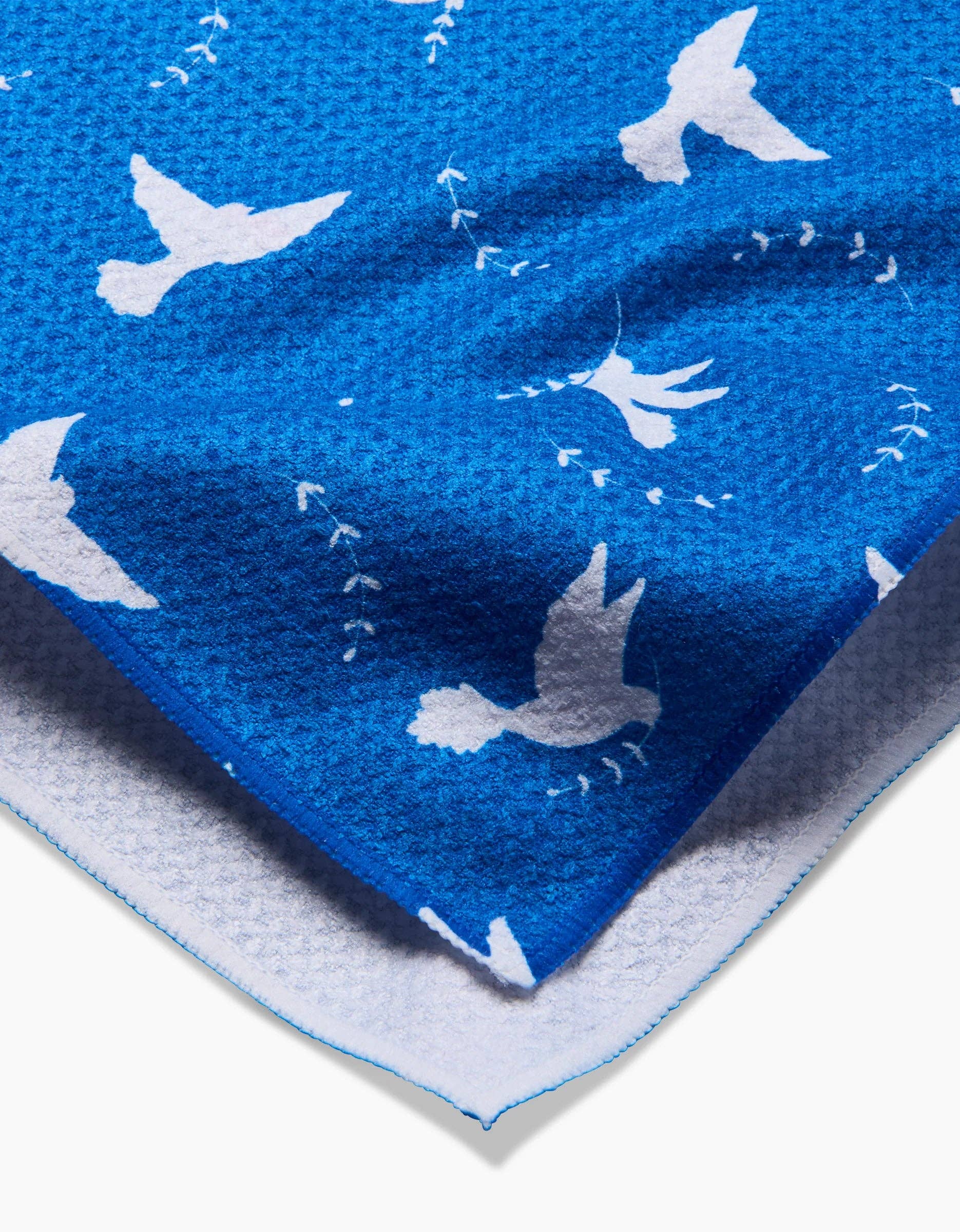 A blue kitchen tea towel with a white peace dove pattern.