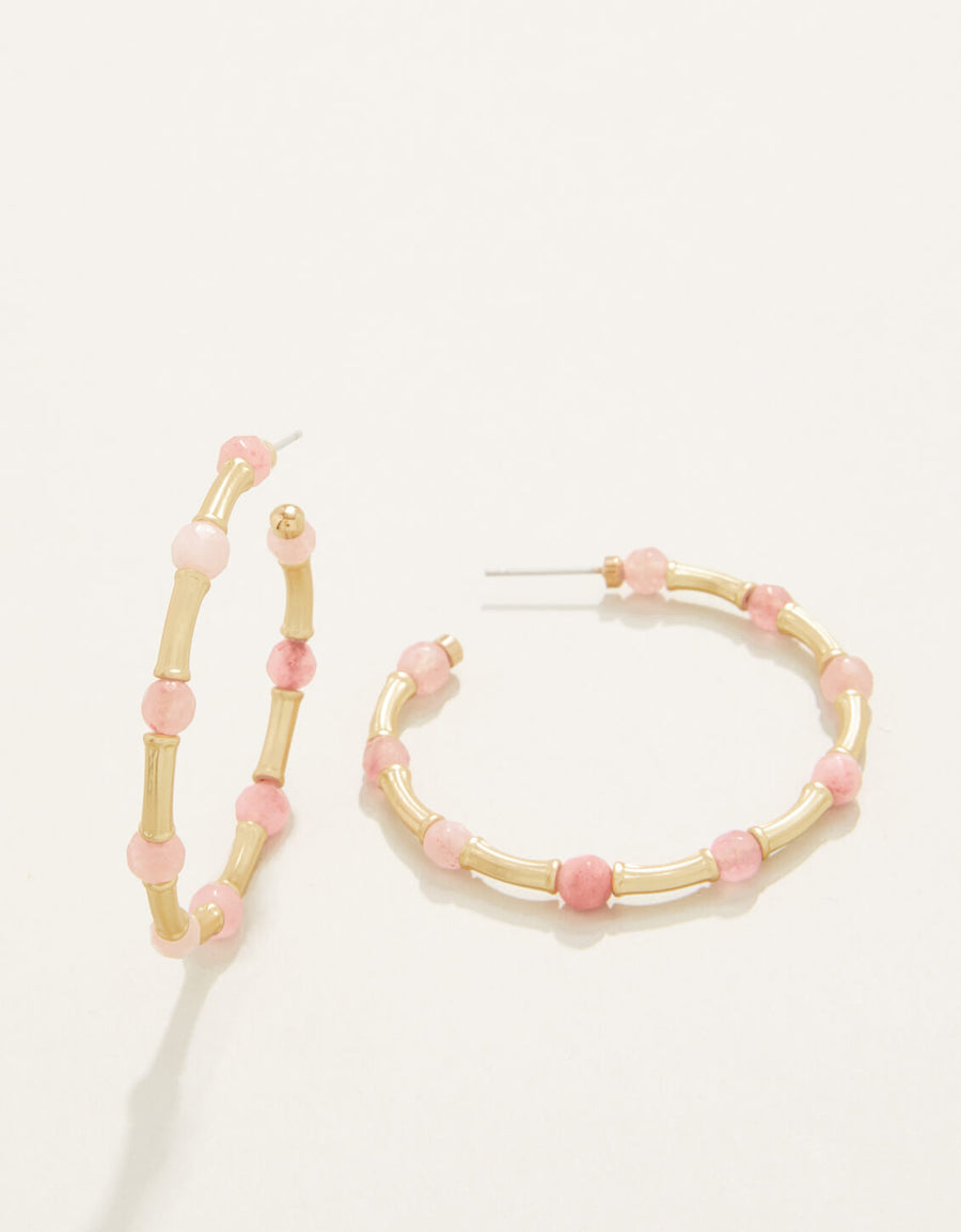 A pair of gold-colored hoop earrings with pink beads attached to them, displayed against a white background.