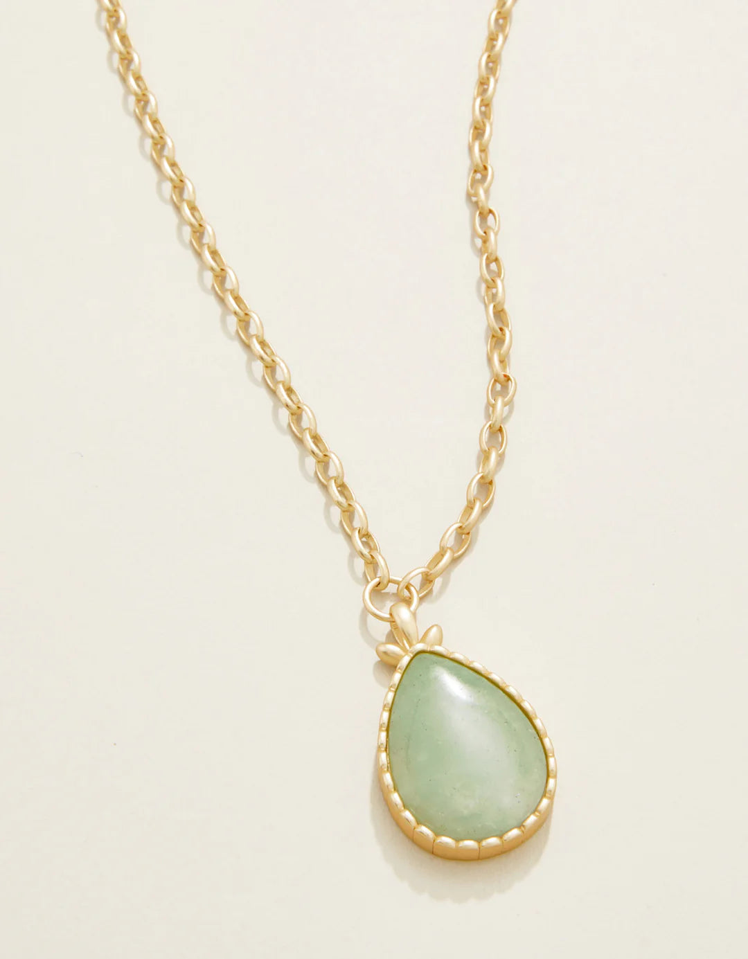 Gold necklace with a green teardrop pendant on a light beige background