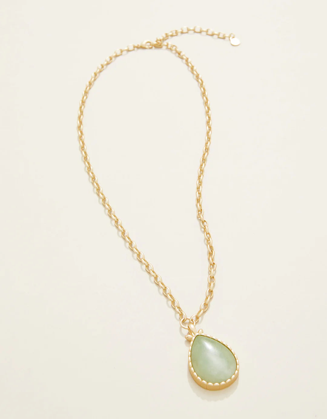 Necklace with a green teardrop pendant on a light beige background