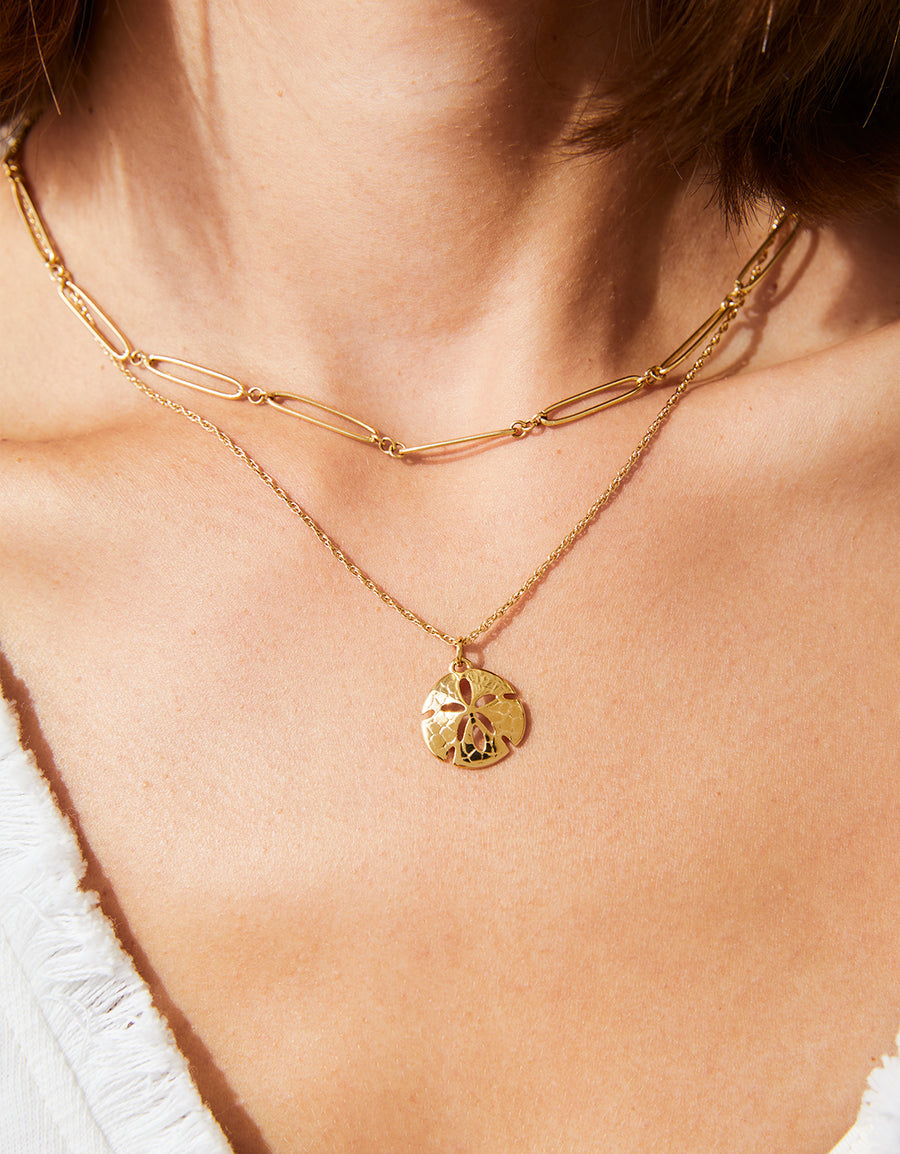 Gold necklace with a pendant on a person wearing a white top.