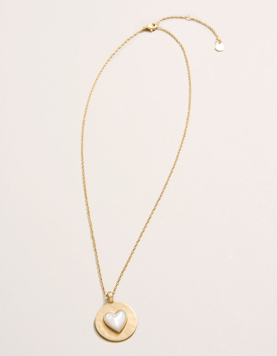 Gold necklace with a heart pendant on a light beige background