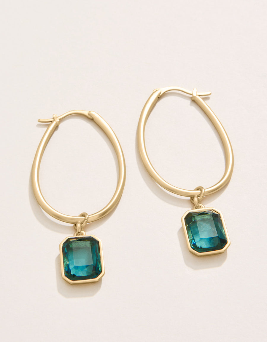 Gold hoop earrings with green gemstones on a light beige background