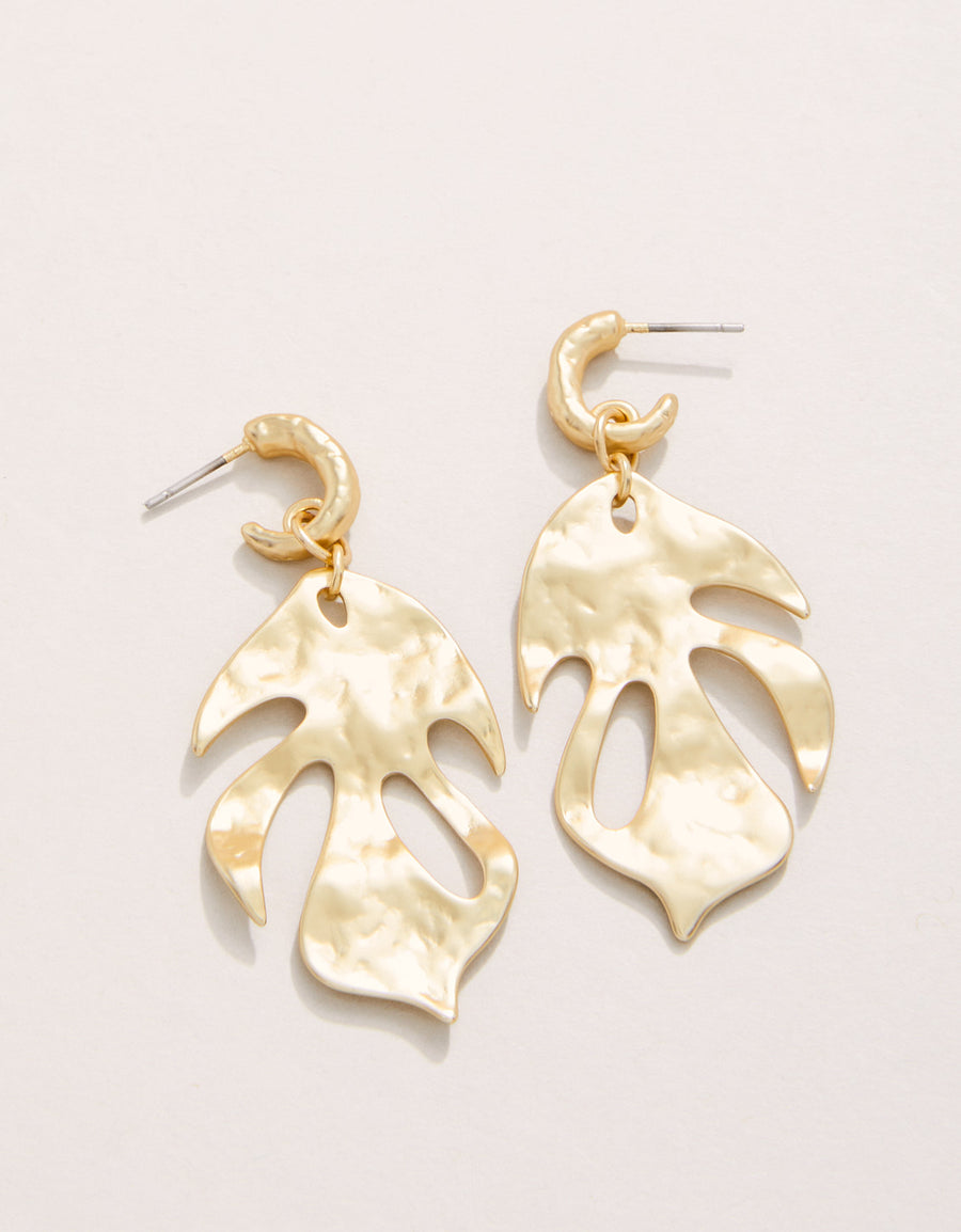 Gold leaf-shaped earrings on a light beige background