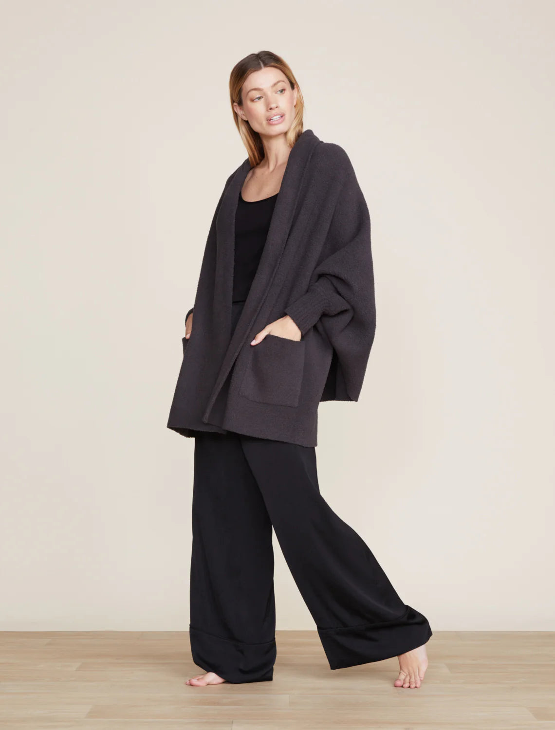 A model wearing a black CozyChic Blanket Wrap with ribbed cuffs and front patch pockets, standing on a plain background.