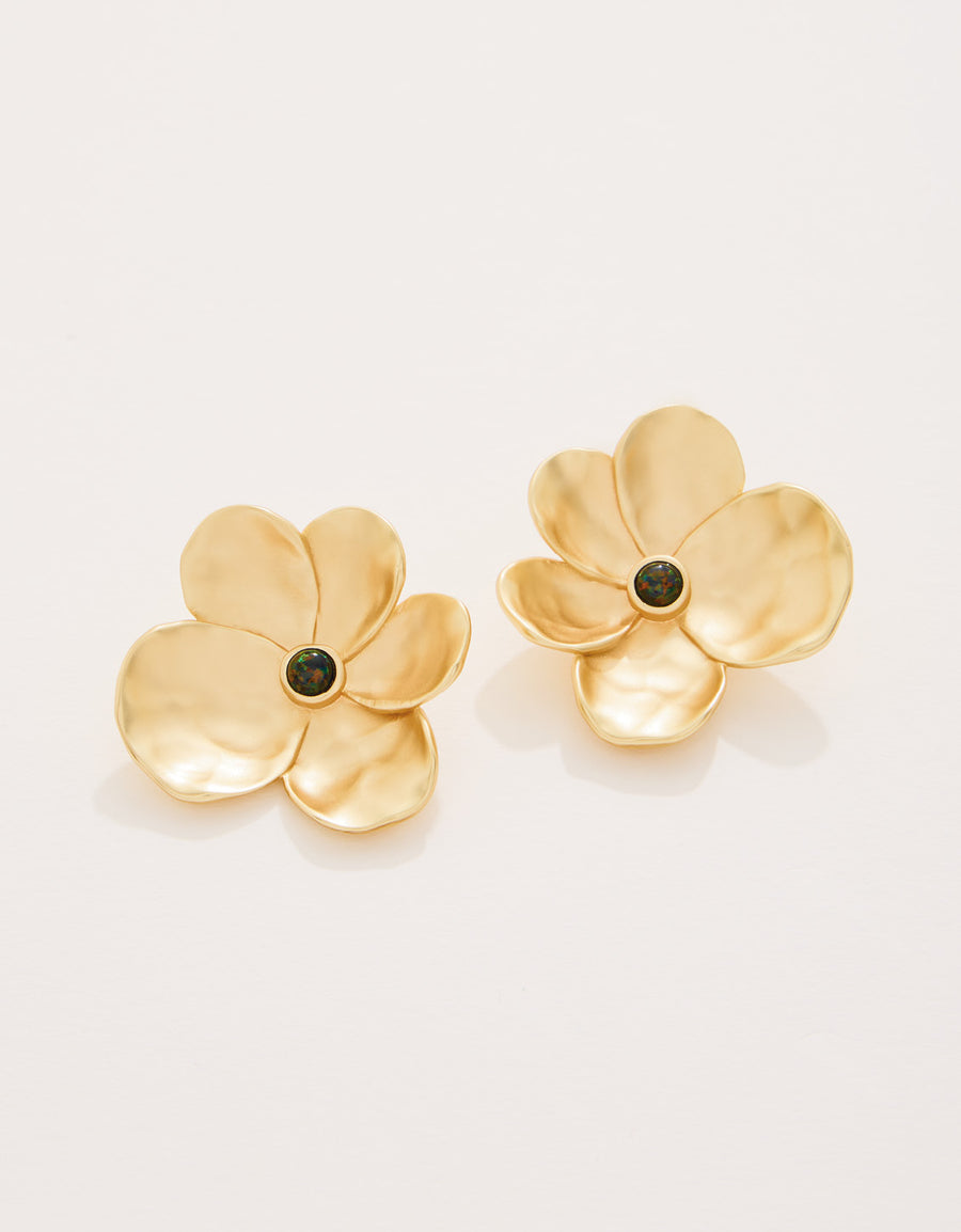 Gold flower-shaped earrings with black centers on a light beige background