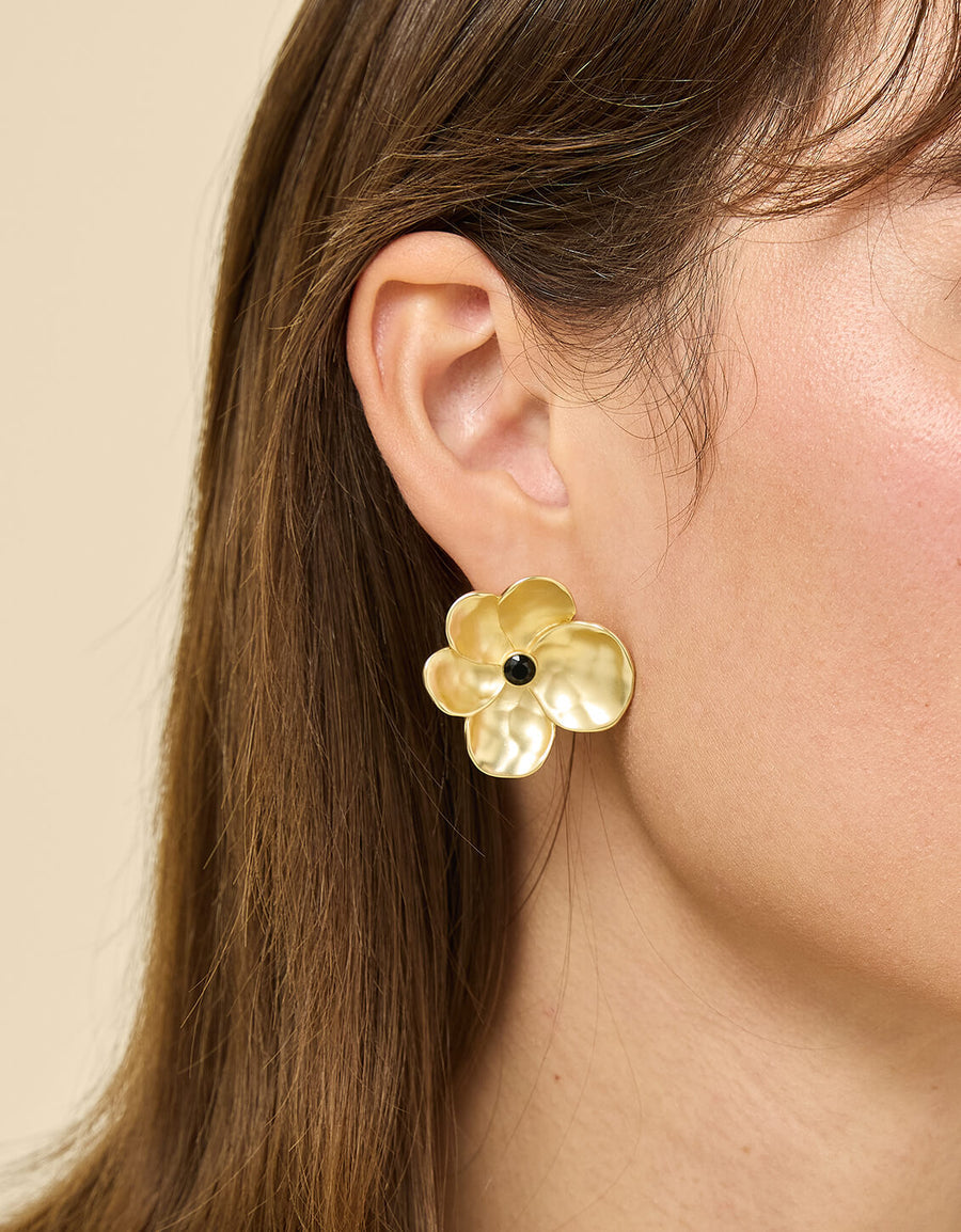 Gold flower-shaped earring worn by a person with a neutral background