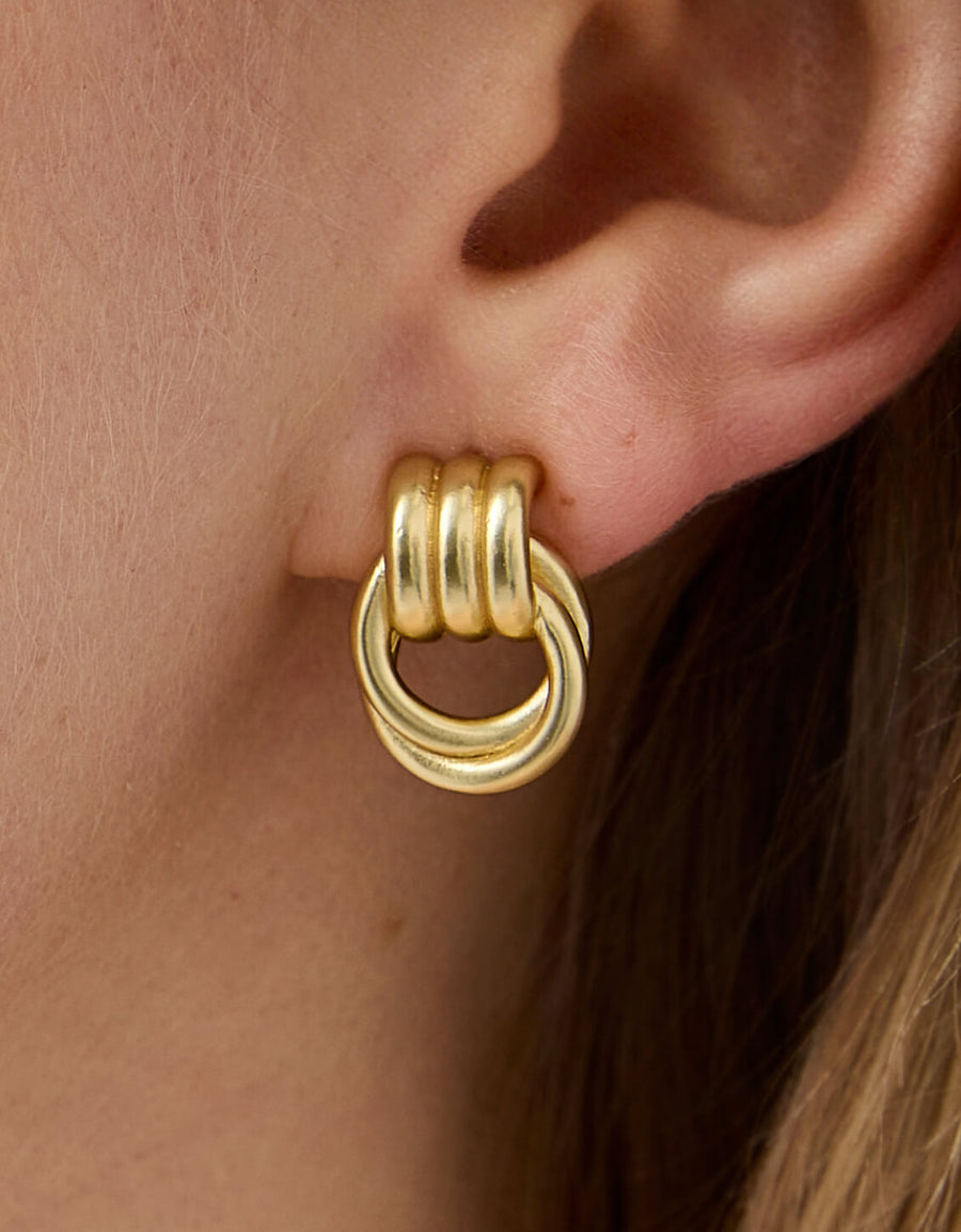 Gold earring worn on an ear with a neutral background