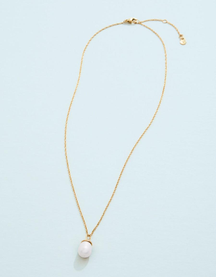 Gold necklace with a pink pendant on a light blue background