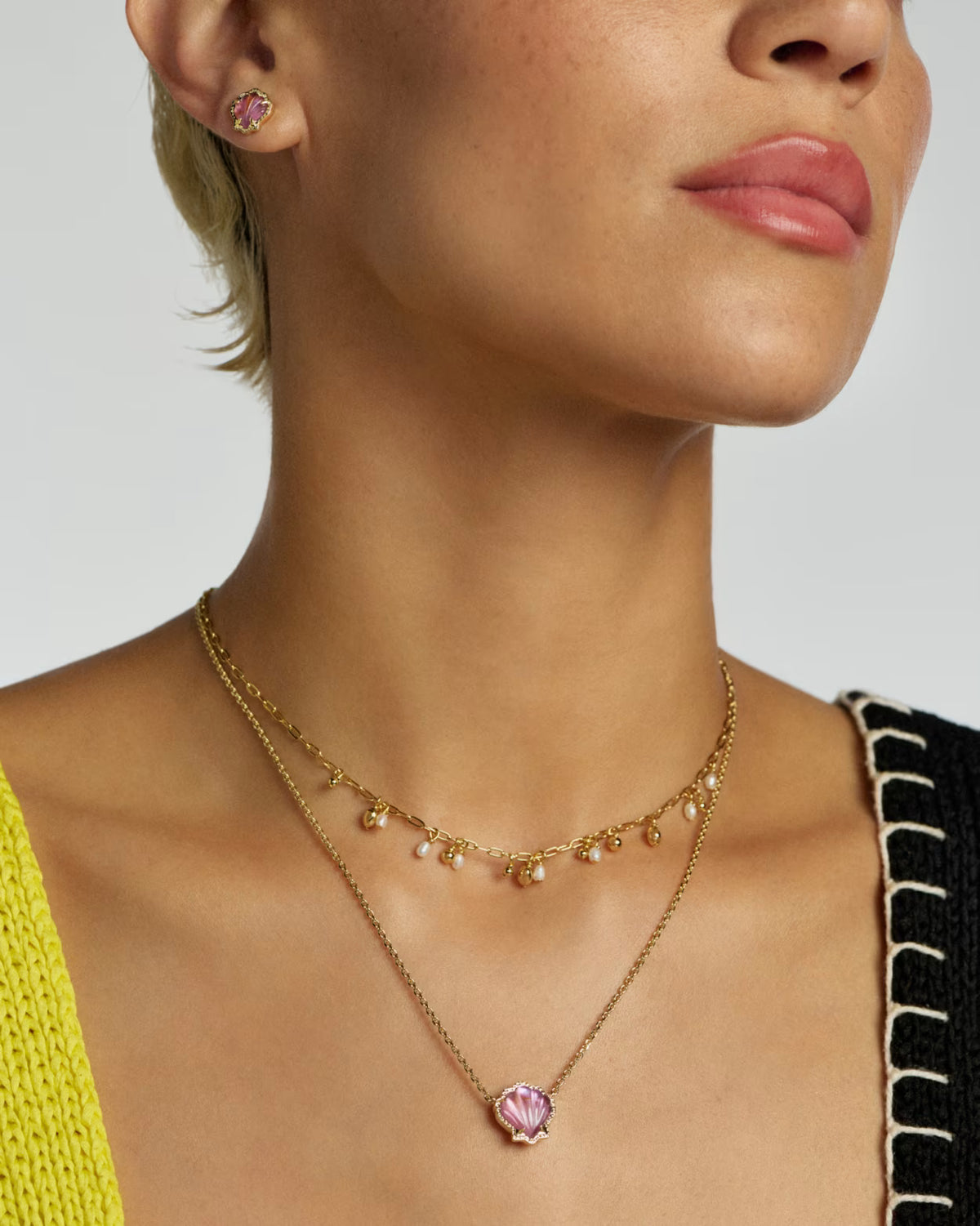 Close-up of a woman wearing a gold necklace with a pink pendant on a neutral background