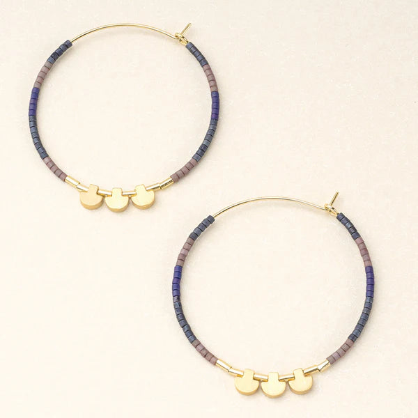 A pair of large hoop earrings with blue and purple beads and gold accents on a white background.