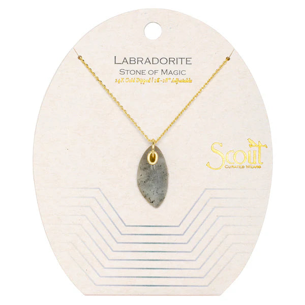 A uniquely shaped organic stone necklace with a gold chain and brass grommet, presented on a card with 'Labradorite Stone of Magic' text and the brand 'Scout'.