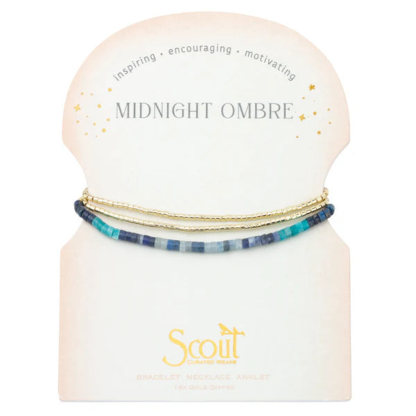 A bracelet wrap with semi-precious gemstones in shades of midnight and gold, packaged in a clear box with the brand name 'Scout'.