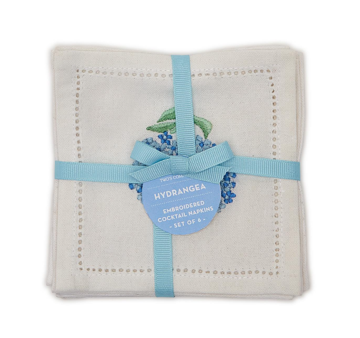A set of six white cotton cocktail napkins with a hydrangea embroidery design, tied together with a blue ribbon.