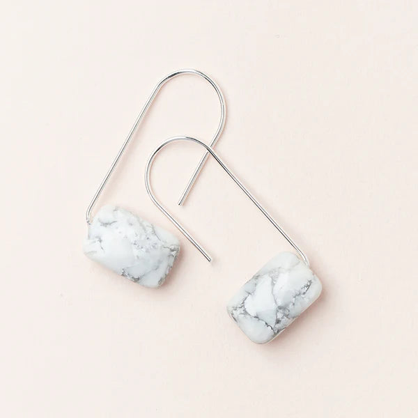 A pair of silver-colored earrings with a marble-like pattern, displayed against a light pink background.