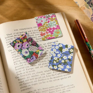 Floral bookmarks on an open book with a pen on a wooden surface