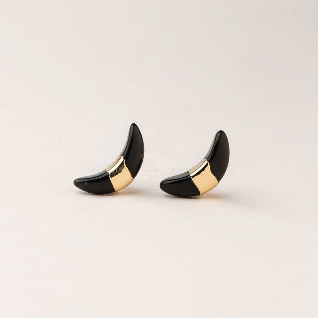 A pair of black spinel crescent stud earrings with a gold foil band on a light beige background.