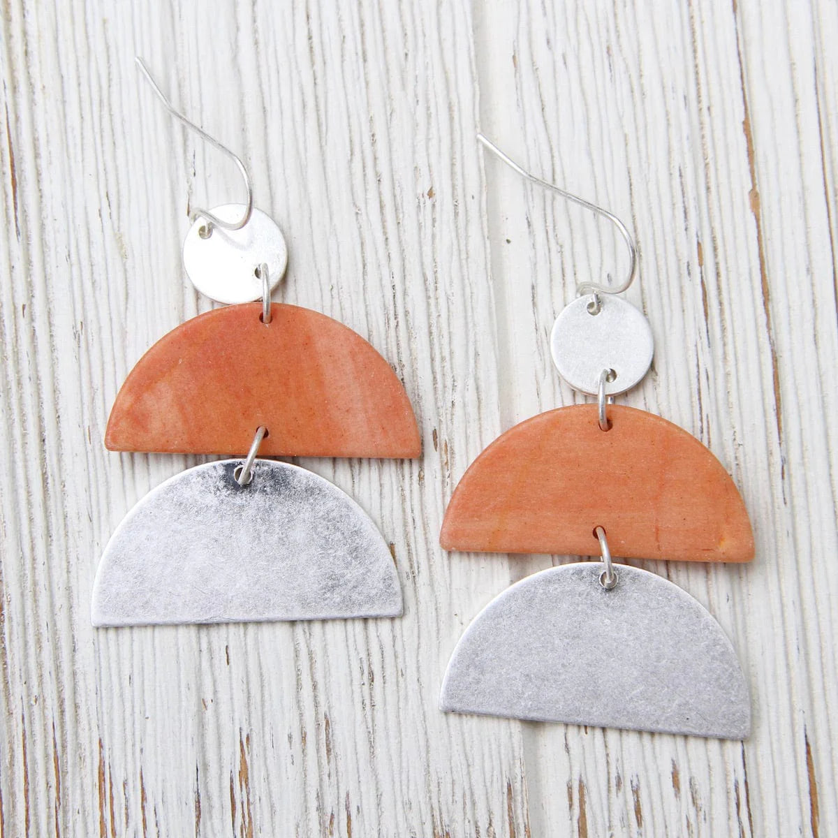 Pair of earrings with orange and silver half-circle design on a wooden surface
