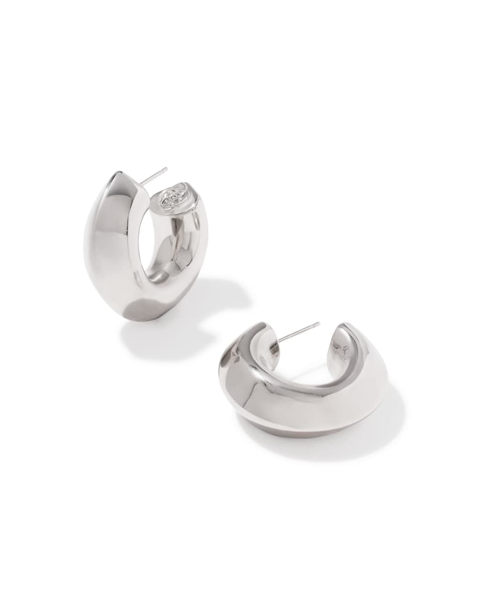 A pair of polished silver huggie hoop earrings with a small clear crystal accent on one earring, displayed on a clean white background.