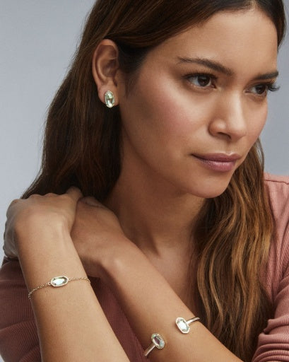 Woman wearing gold jewelry including earrings and a bracelet on a neutral background