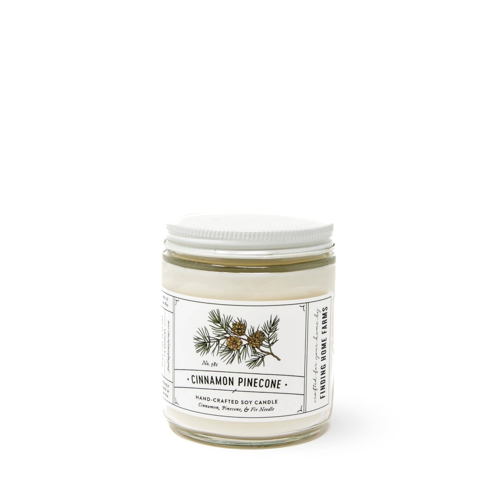 A glass jar candle with a white screw-top lid and a white paper label reading 'CINNAMON PINECONE' shown on a clean white background.