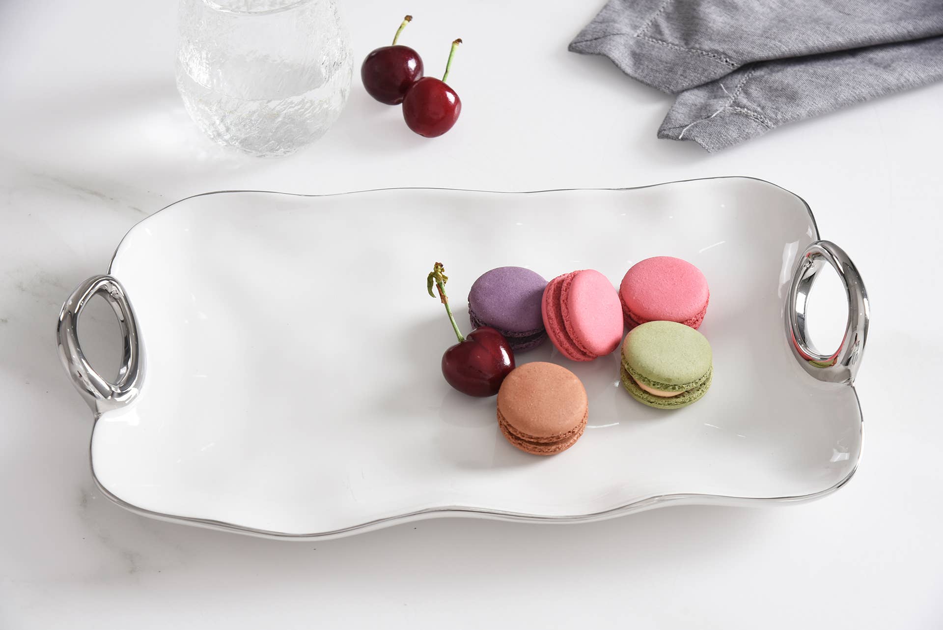Rectangular silver tray with colorful macarons and cherries on a white surface.