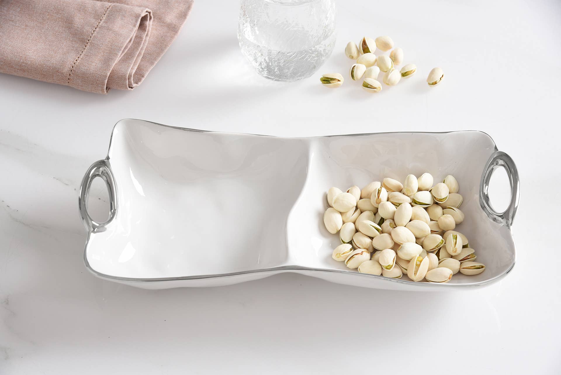 White ceramic dish with two compartments filled with almonds on a marble surface.