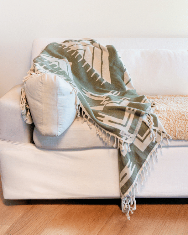 Green patterned blanket draped over a white couch with a wooden floor.