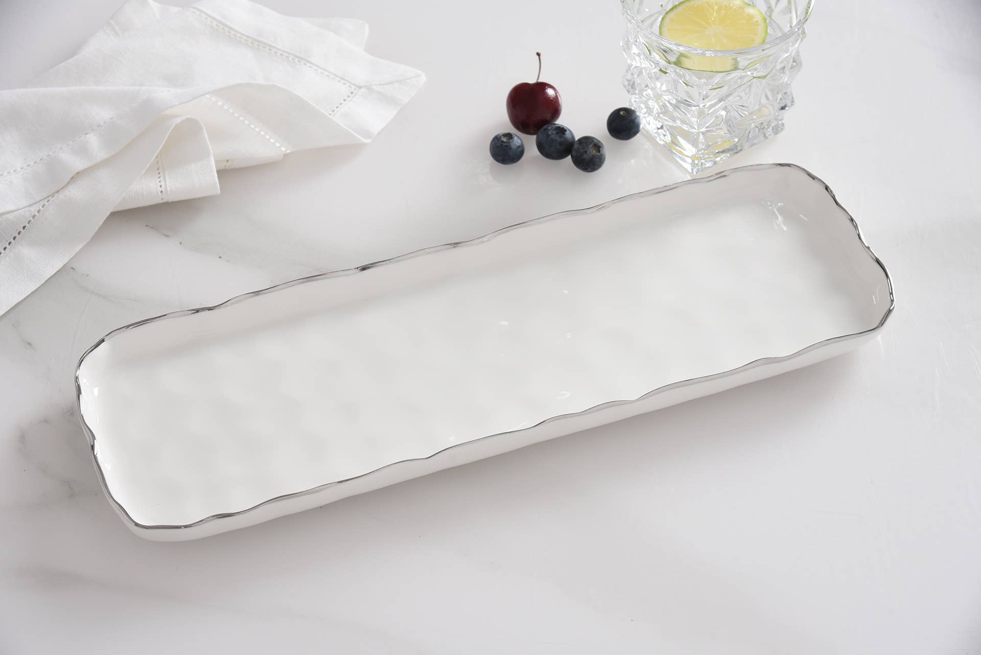 Rectangular white ceramic tray on a light surface with cherries and a glass of water.