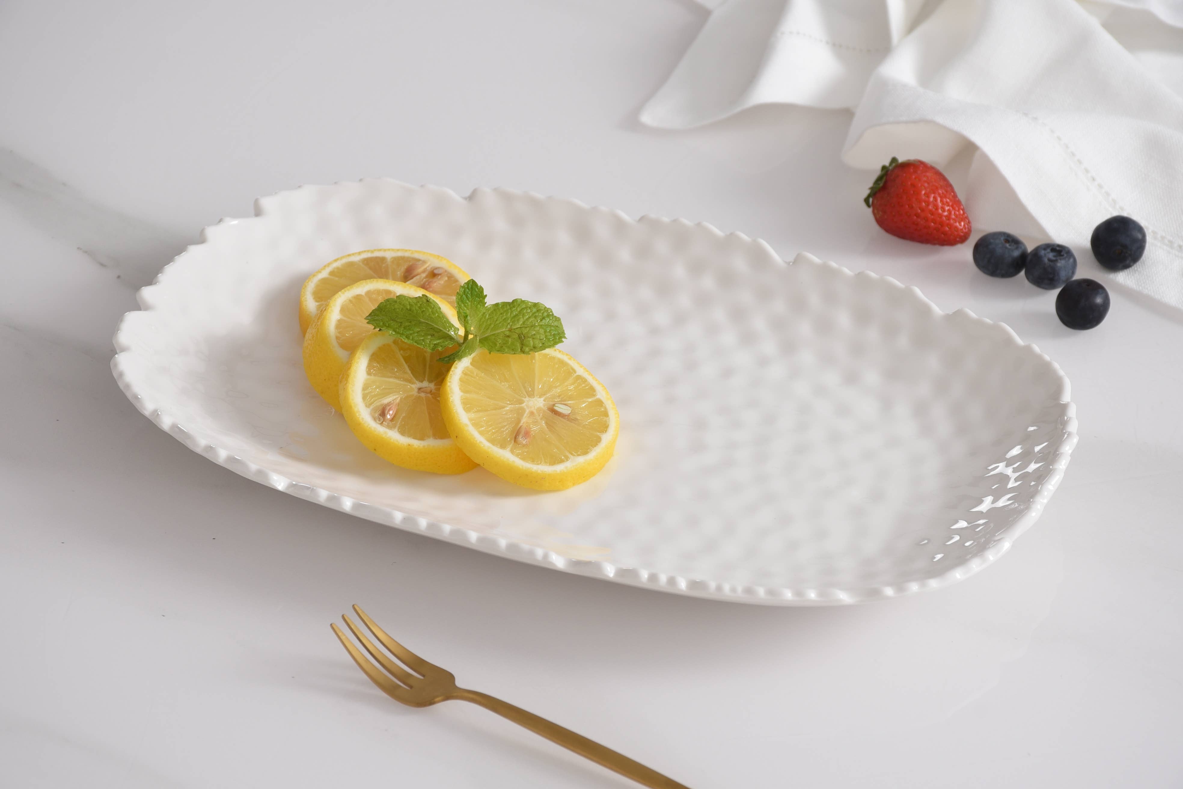 White decorative plate with lemon slices and mint leaves on a white surface with a gold fork.