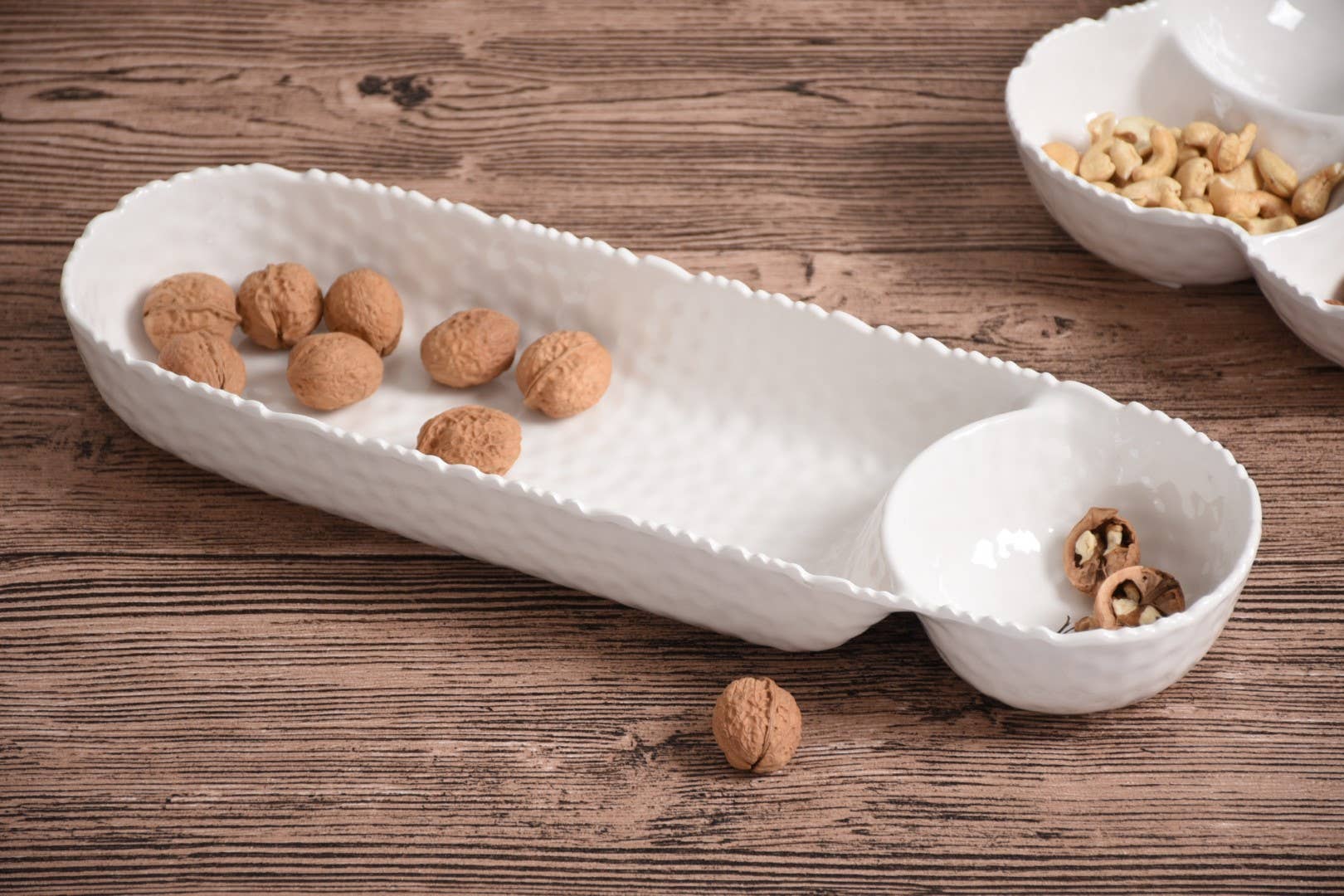 White ceramic tray with small bowls on a wooden surface, containing nuts.