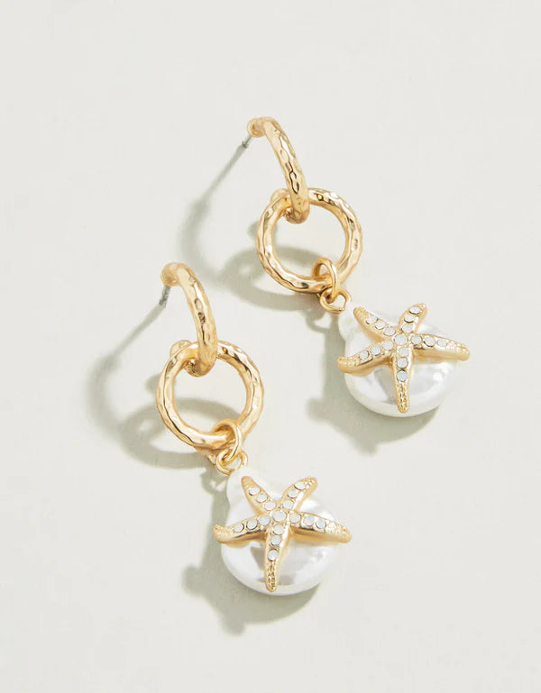 A pair of earrings featuring gold-colored posts and white faux pearl embellishments with white opal glass crystals, displayed against a light background.