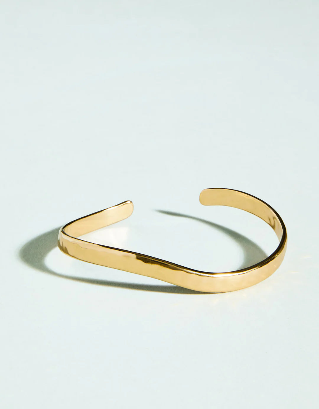 Gold open cuff bracelet on a light blue background