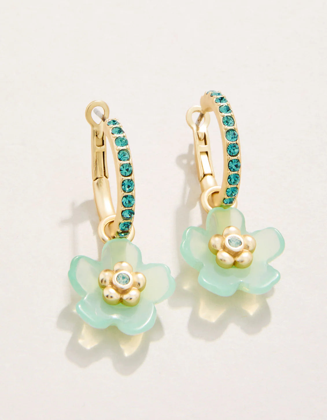 A pair of gold-plated earrings featuring a lever back post hoop closure with a floral design in sea foam green color, adorned with blue-green crystals.